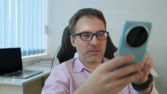 Businessman scrolling through news or social media on his smartphone while resting with feet up. Office relaxation and digital leisure. scrolling news