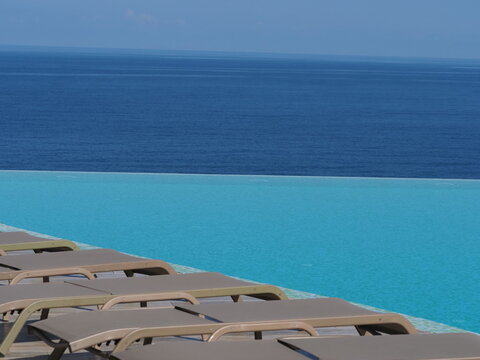 View of the infinity pool with sun loungers against the backdrop of the sea, and the hotel grounds.