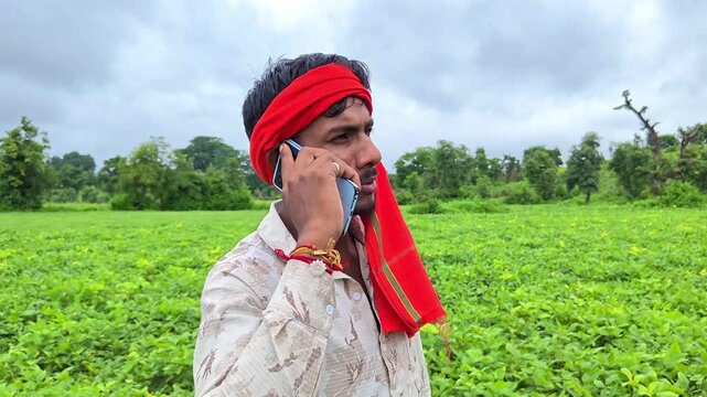 Young indian farmer talking on mobile phone in green agriculture field. Smart farming and digital agriculture concept