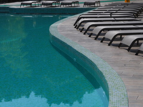 View of the infinity pool with sun loungers against the backdrop of the sea, and the hotel grounds.