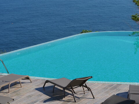 View of the infinity pool with sun loungers against the backdrop of the sea, and the hotel grounds.