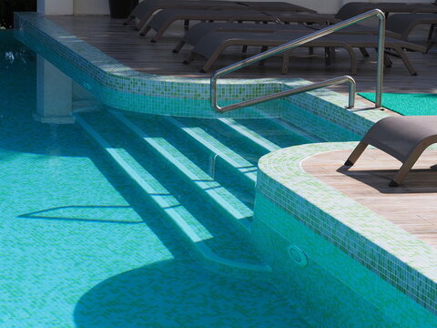 View of the infinity pool with sun loungers against the backdrop of the sea, and the hotel grounds.