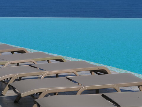 View of the infinity pool with sun loungers against the backdrop of the sea, and the hotel grounds.