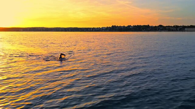 A swimmer battles gentle waves against a vibrant sunset, embodying determination and challenge. Focused strokes highlight rigorous training essential for triathlon.
