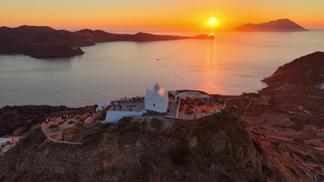 Sunset on a Greek island, aerial view, orbiting drone shot of traditional whitewashed church on a cliff overlooking Aegean Sea in Greece, spectacular sunset on Milos islands, vacation in the Cyclades
