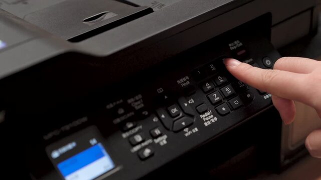 Hand operating control panel of a black office printer on a wooden desk