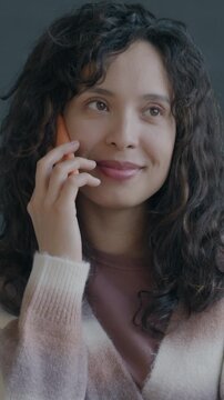Cheerful Middle Eastern lady speaking on mobile phone smiling enjoying call on black background. People and cellphone communication concept.