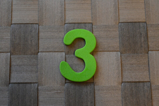 Green number three on a woven brown background