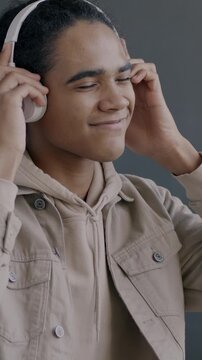 Slow motion portrait of cheerful African American guy listening to music through headphones dancing on black background. People and modern lifestyle concept.