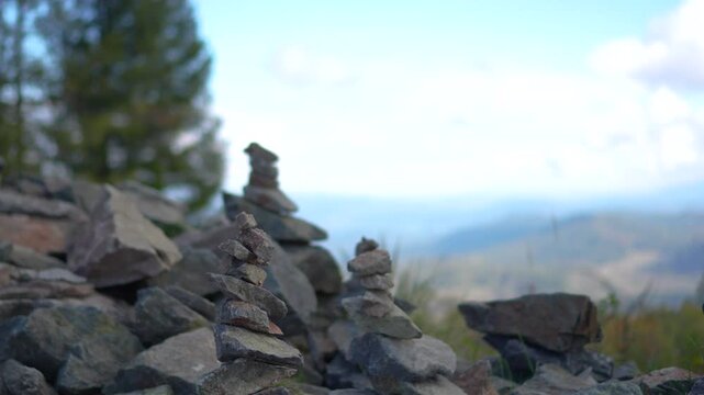 Close up of balanced stone pyramids on a mountain peak with a slow camera push in and focus pull revealing a vast alpine valley