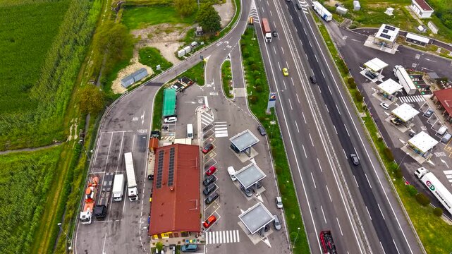 Aerial view hyperlapse showing continuous vehicle movement on the A50 motorway and activity around a roadside service area, highlighting transport infrastructure. Italy, Milan