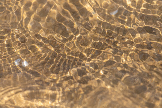 Golden sunlight ripples over shallow sandy water creating abstract shimmering patterns and warm reflections