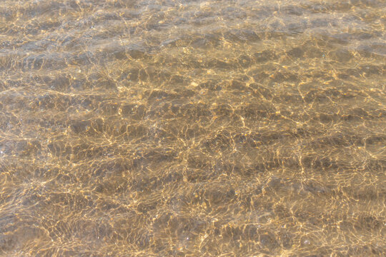Golden sunlight on shallow beach water with rippled sand and sparkling reflections