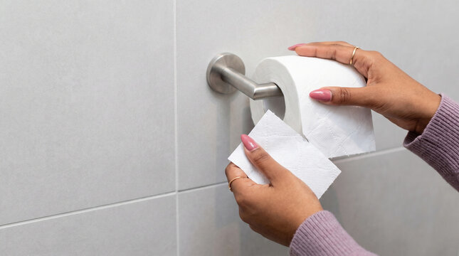Hands tearing toilet paper from roll on bathroom wall holder