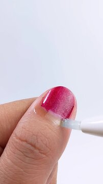Close up of applying clear moisturizing liquid on thumb nail that already has purple nail polish. Nail care treatment, beauty and wellness concept isolated on white background.