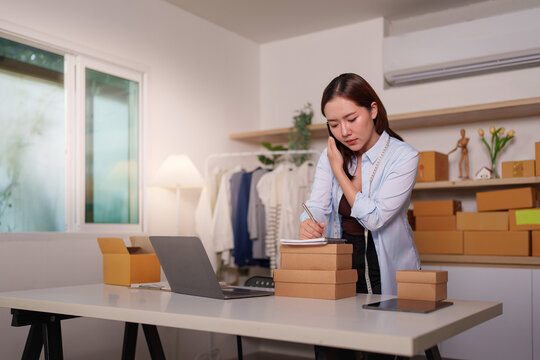 Asian small business owner taking phone order notes while managing e-commerce sales