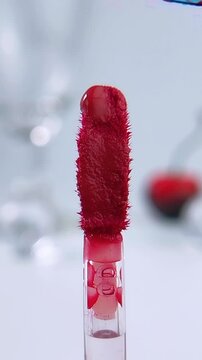 Red liquid being arranged to flow on the brush tip. Beauty product introduction concept for makeup or lip tint cosmetic application.