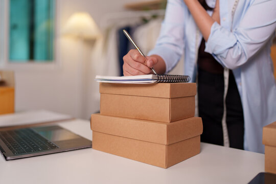 Cropped hand writing order notes in notebook on cardboard box for e-commerce business