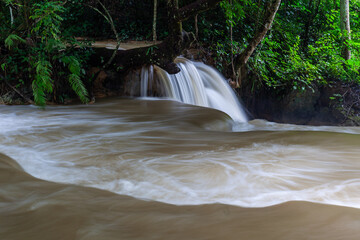 Waterfall cascades over rocks in a dense tropical forest of Laos, muddy brown water flowing into a frothy pool. © Eugene Ga
