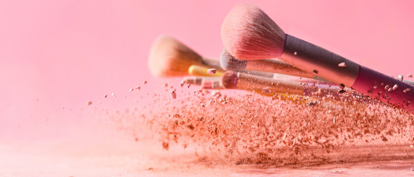 Make up brushes with powder splashes isolated on pink background