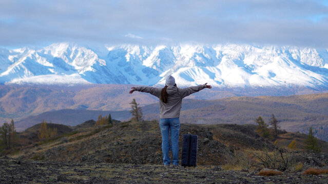 Rear view of a female tourist with arms wide open enjoying scenery of snow capped Altai mountains in autumn.