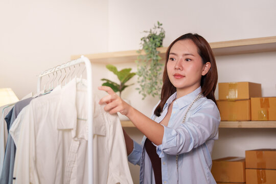 Asian female entrepreneur checking clothes on rack for e-commerce small business