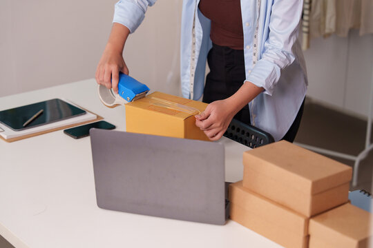 Cropped hands sealing cardboard package with tape dispenser for e-commerce delivery