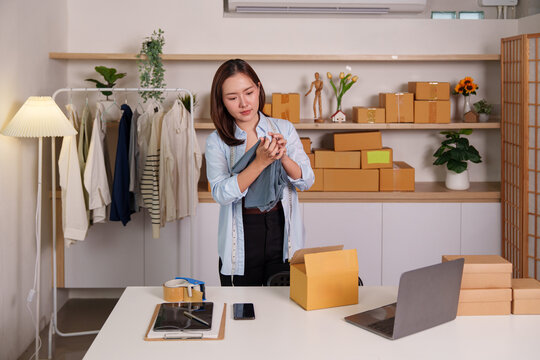 Asian woman small business owner inspecting clothing for e-commerce store order fulfillment