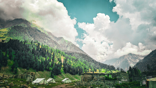 Camping tents in a lush green mountain valley under a cloudy sky with copy space