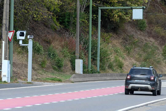 une voiture noire circule sur une route en agglom&eacute;ration en Belgique et sa vitesse est contr&ocirc;l&eacute;e par un radar tachym&egrave;tre automatique avec cam&eacute;ra install&eacute; en haut d'une poteau 