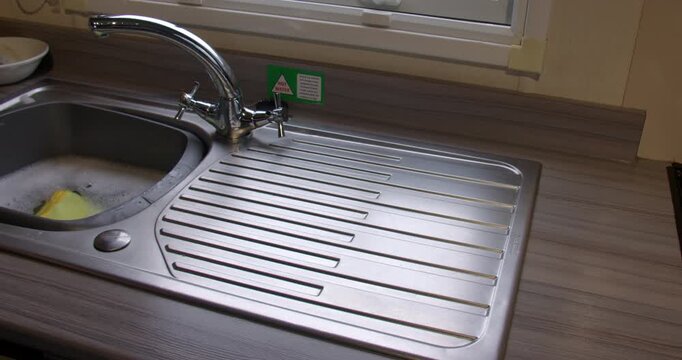 Man finishing up washing up and drying plates and cutlery and wiping down the sides inside a static caravan