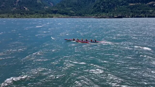 A slow motion aerial drone shot circling a six person canoe team paddling their canoe with an outrigger in the windy and wavy waters of the Columbia River Gorge during a competition