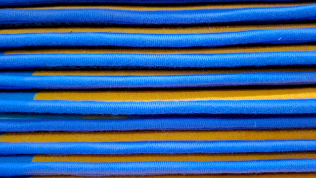 Close up background of stacked blue and yellow fabric floor mats, showing folded edges and smooth textile texture in horizontal pattern.