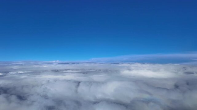 Pilot view from a jet cockpit while flying peacefully over an endless blanket of stratus clouds under a blue sky.