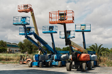 Group of self propelled telescopic hydraulic boom lifts with raised working platforms and baskets parked on construction machinery yard. © Ekaterina