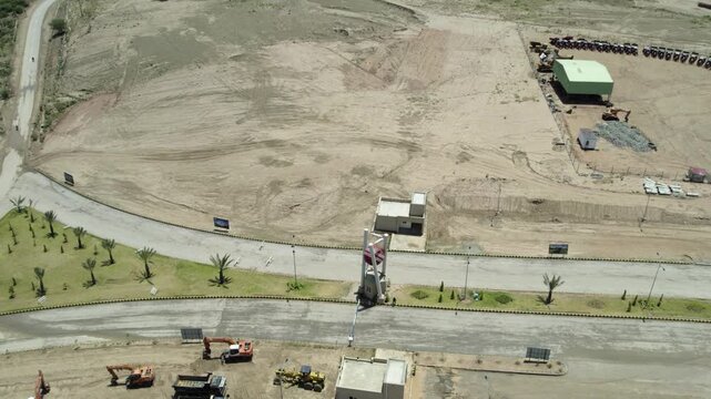 Parked construction vehicles and paved roads border a broad graded development site in Pakistan