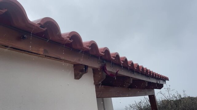 Horizontal view of water dripping from broken gutter pipe on roof edge causing wood beam damage during heavy rainy day needing repair. High quality 4k footage