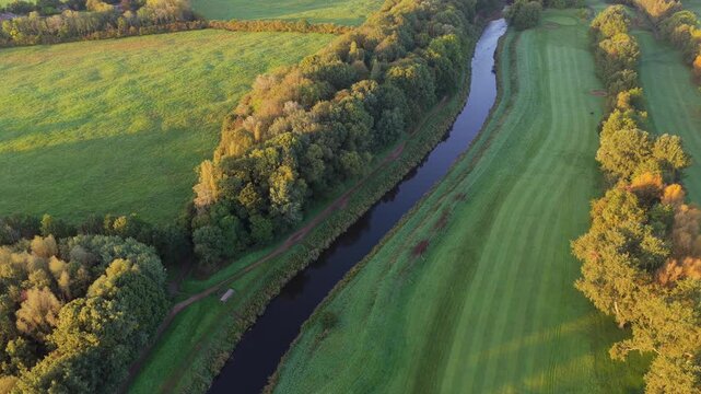 Aerial video capturing the blue River Mersey meandering past Didsbury Golf Course fairways, Stenner Woods, and dewy Millgate Fields at sunrise.