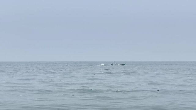 People riding on a fast speed boat cutting through calm sea waves on a hazy day.