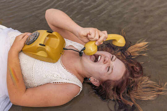 Teenage girl lying on beach screaming into vintage yellow telephone