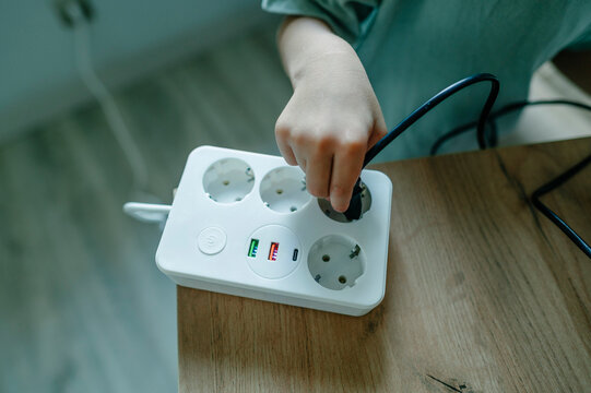 Child holds a black plug near a white electrical outlet indoors