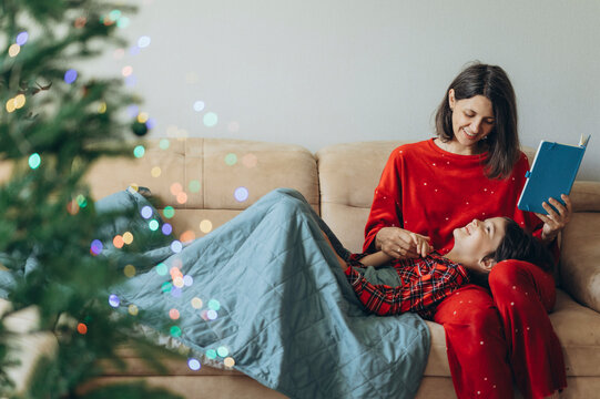 Mother reads a book to her son on the sofa at Christmas time