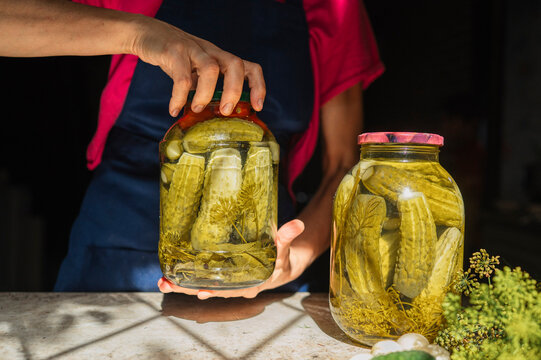 Mature woman prepares pickled cucumbers in glass jars for winter