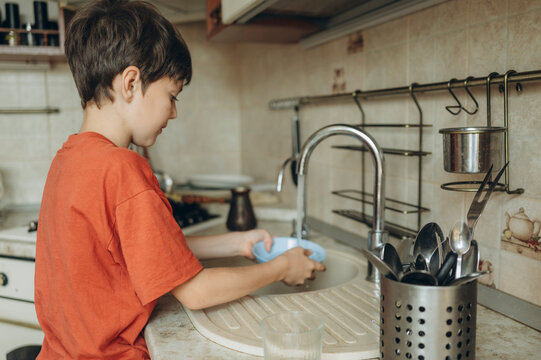 Boy washing breakfast bowl in kitchen sink at home