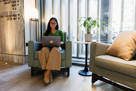 A smiling businesswoman works on a laptop in a hotel lobby