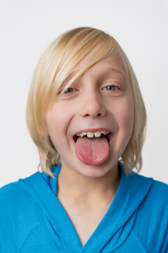Playful child with blonde hair sticking out a tongue, making a funny and silly expression while looking at the camera on a white background