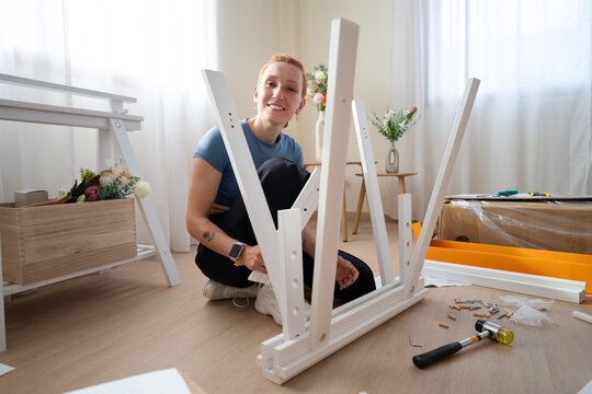 Smiling woman assembles wooden furniture frame on the floor at home