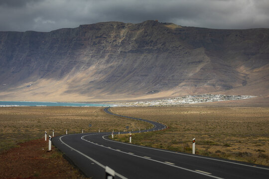 A winding road leads to Famara village under volcanic cliffs