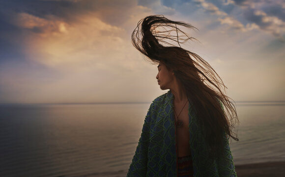 Man in caftan watches the sea at sunset with hair blowing in wind