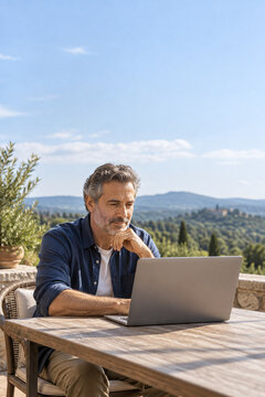 Mature man using a laptop on a terrace with mountain views